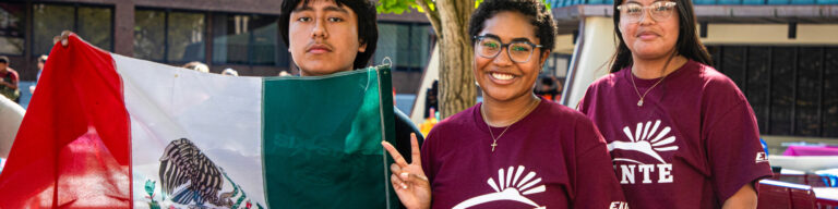 three EKU students pose outside while one holds the flag of Mexico