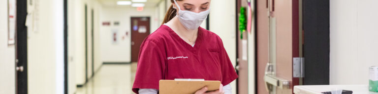 an EKU nursing student wears a mask in a hospital hallway as she looks at a clipboard