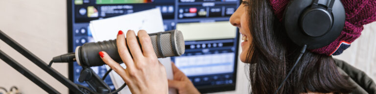 a smiling student wears headphones and speaks into a microphone while using a broadcast program on a computer