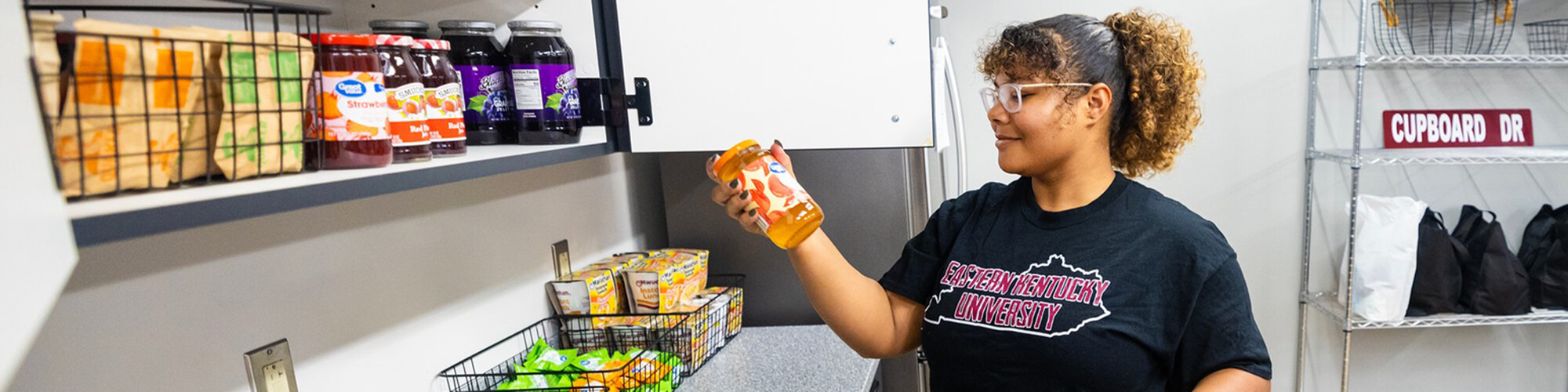 A female EKU student reads the label of a jar of jam as gathers food in Colonel's Cupboard.